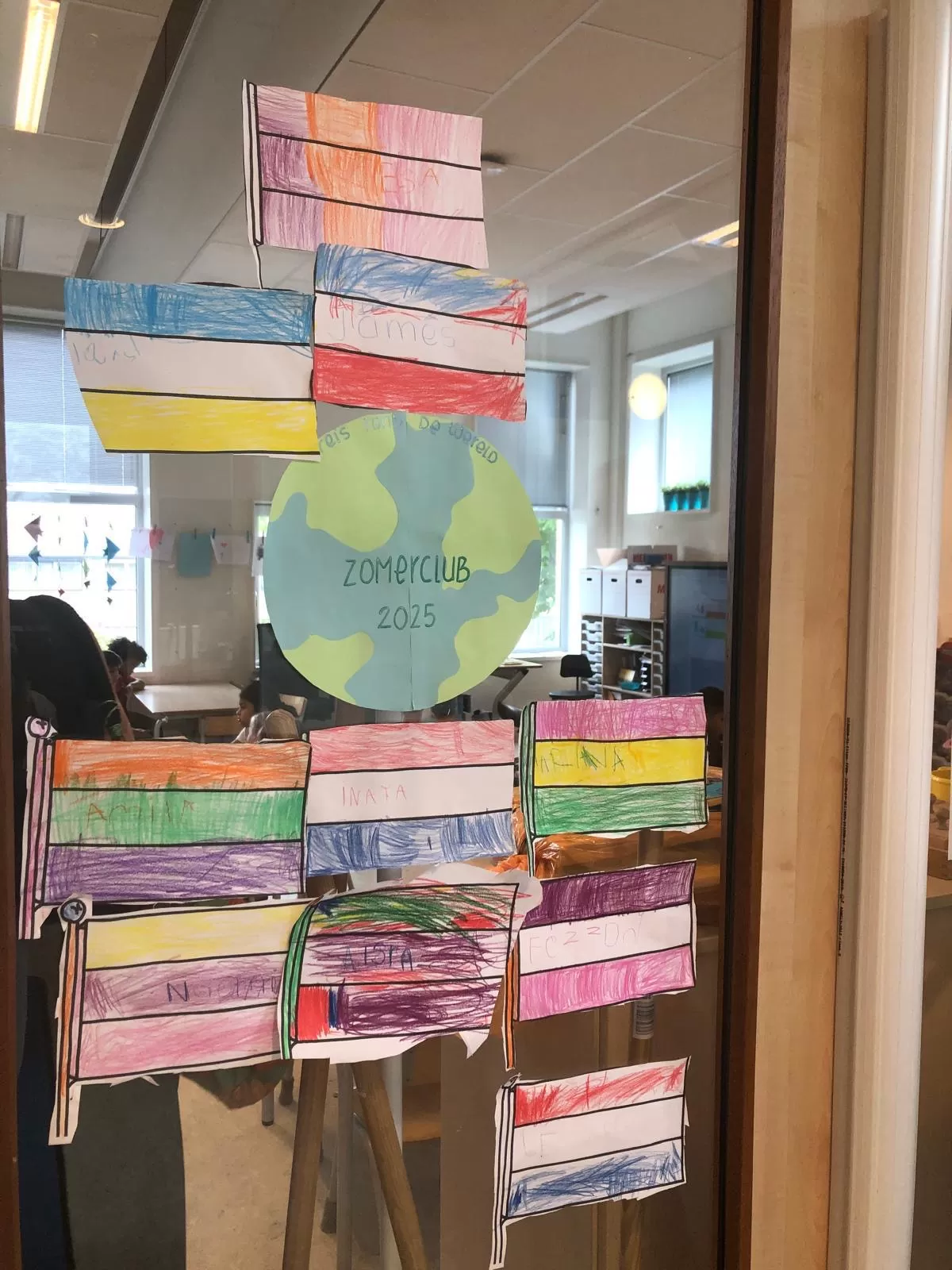 Vlaggen ingekleurd door kinderen en een wereldbol met de tekst 'Zomerclub 2025'