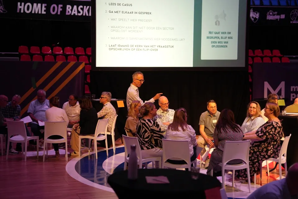 Groepen mensen in een zaal die kringgesprekken voeren
